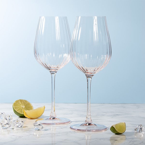 Two clear stemmed wine glasses on a light marble surface with lime wedges, ice cubes, and a pale blue background.