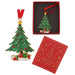 A Christmas tree ornament shown alongside its red gift box and a red branded insert card. The ornament is green with gold trim, red ornaments, a gold star, and small wrapped presents beneath it.