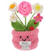 A crocheted flower pot plush toy with a smiling face and a message for 'Mum', featuring a pink pot, green stems, a large pink rose, white and yellow daisies, a small pink flower, a ladybug, and a red strawberry on a white background.