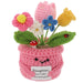 A crocheted flower pot with handmade yarn flowers in pink, blue, yellow, white, and green leaves, featuring a cute embroidered face and a message card that reads 'Daughter, you make my heart grow'.
