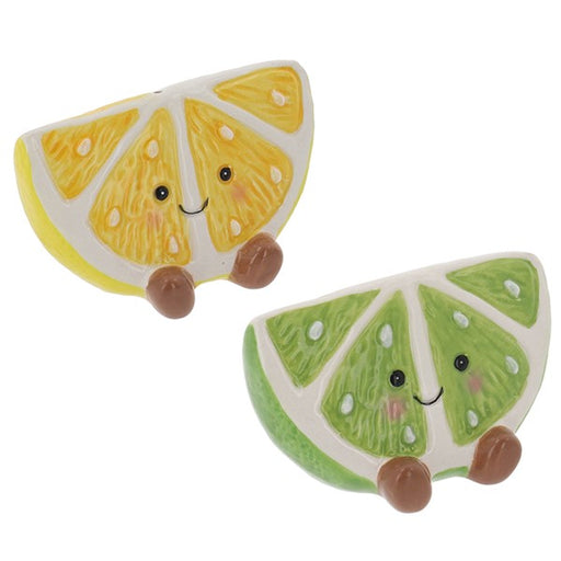 Two cute, cartoonish ceramic fruit slice figurines on a plain white background. One is a yellow citrus slice with a smiling face, and the other is a green lime slice with a smiling face.
