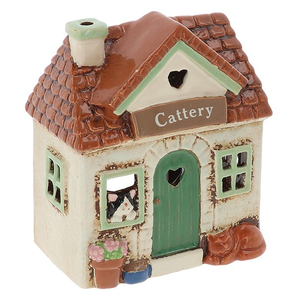 A ceramic cottage-shaped cattery shop ornament with a brown tiled roof, cream-colored walls, a green door, and a sign reading 'Cattery' on the front.