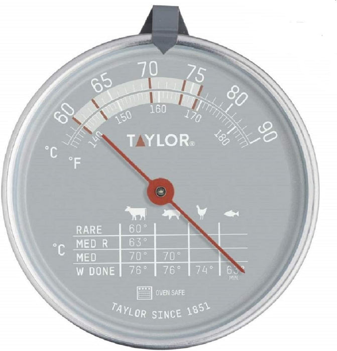 A round Taylor oven-safe thermometer with a silver metallic face and rim, featuring dual temperature scales in Celsius and Fahrenheit, a red needle, and cooking time/temperature guides printed on the dial.