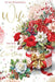 A festive Christmas greeting card design with the text 'To My Wonderful Wife With All My Love At Christmas.' The card features a large bouquet of red and white flowers, green leaves, red berries, and a red-and-white gift box with a gold bow on a white background with decorative snowflake and star accents.