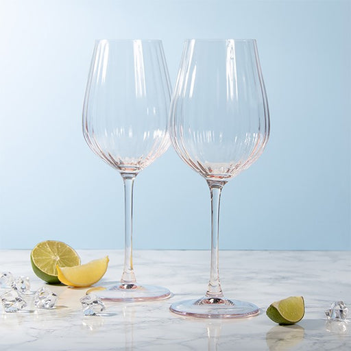Two clear stemmed wine glasses on a light marble surface with lime wedges, ice cubes, and a pale blue background.