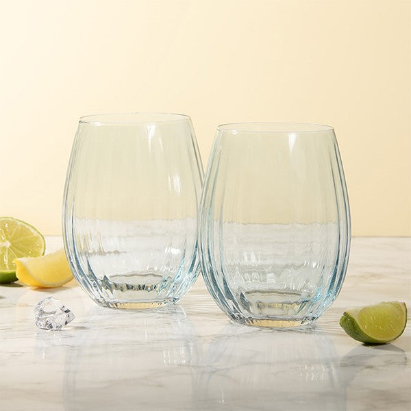 Two clear stemless wine glasses with a textured, ribbed pattern, displayed on a light marble surface with lime slices and ice cubes against a warm cream background.