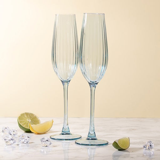 Two clear champagne flutes on a light surface with a lemon and lime wedge in the background.