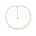 A baroque pearl necklace with a gold chain extender and a small oval gold tag, displayed on a clean white background.