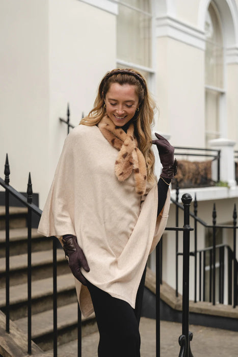 Woman wearing a beige poncho and brown gloves standing on a staircase.