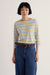 A model wearing a cream-colored long-sleeve boat-neck top with thin yellow and blue horizontal stripes, paired with high-waisted blue jeans and a brown leather belt, against a plain off-white background.
