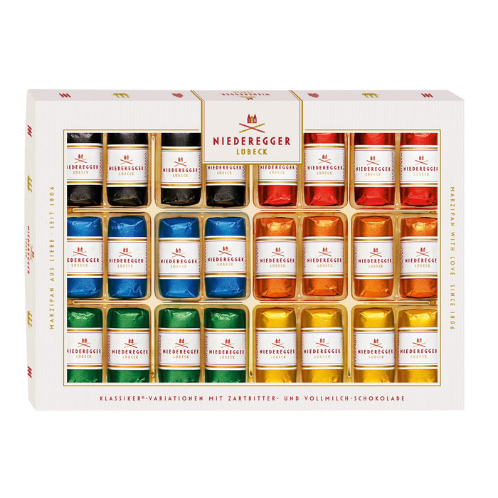 A boxed assortment of Niedergger chocolate tart and milk chocolate pieces in a white gift box with gold trim. The front shows multiple rows of small wrapped pieces in assorted colors including black, blue, green, orange, red, and yellow, with the brand name Niedergger visible on the packaging.