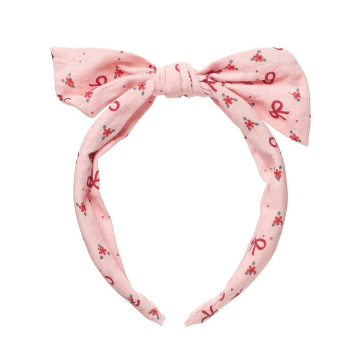 A light pink fabric headband with a large bow at the top and an allover pattern of small red bows and tiny red floral motifs, shown on a plain white background.