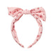 A light pink fabric headband with a large bow at the top and an allover pattern of small red bows and tiny red floral motifs, shown on a plain white background.