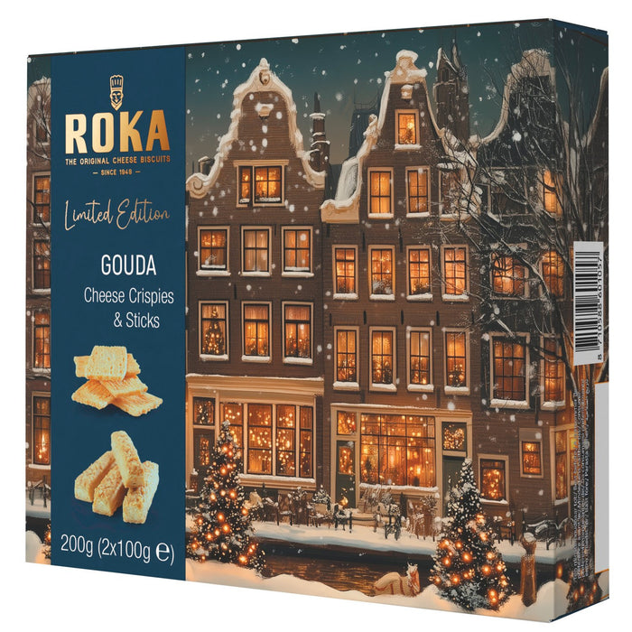 Roka Gouda Cheese Crisps and Sticks limited edition box, featuring a dark blue left panel with product text and biscuit imagery, and a right panel showing a snowy European town scene at night with warm glowing windows.